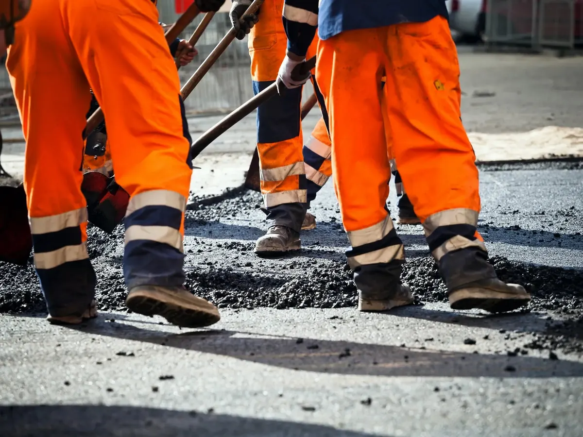 Surfacing crew in hi-vis raking and levelling fresh tarmac