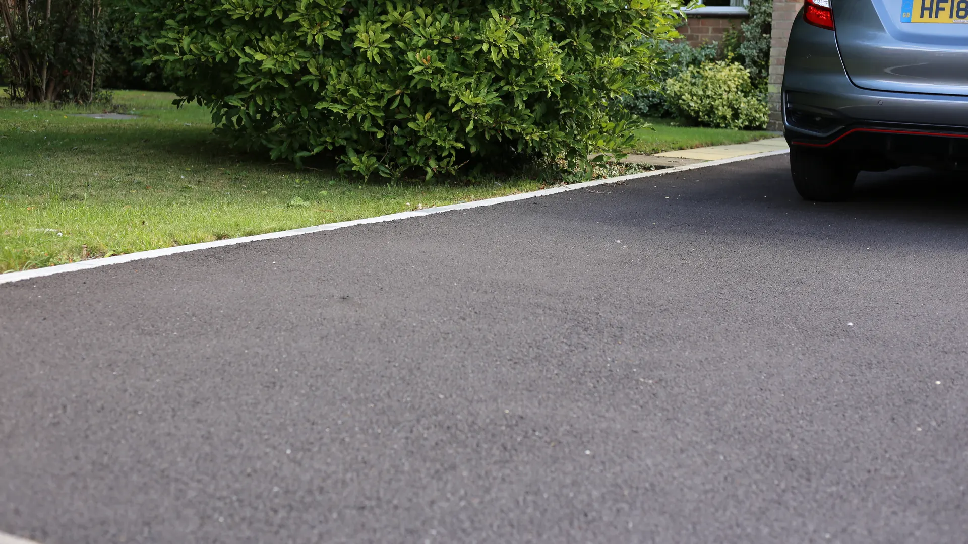 New tarmac driveway edged with a light kerb beside a lawn