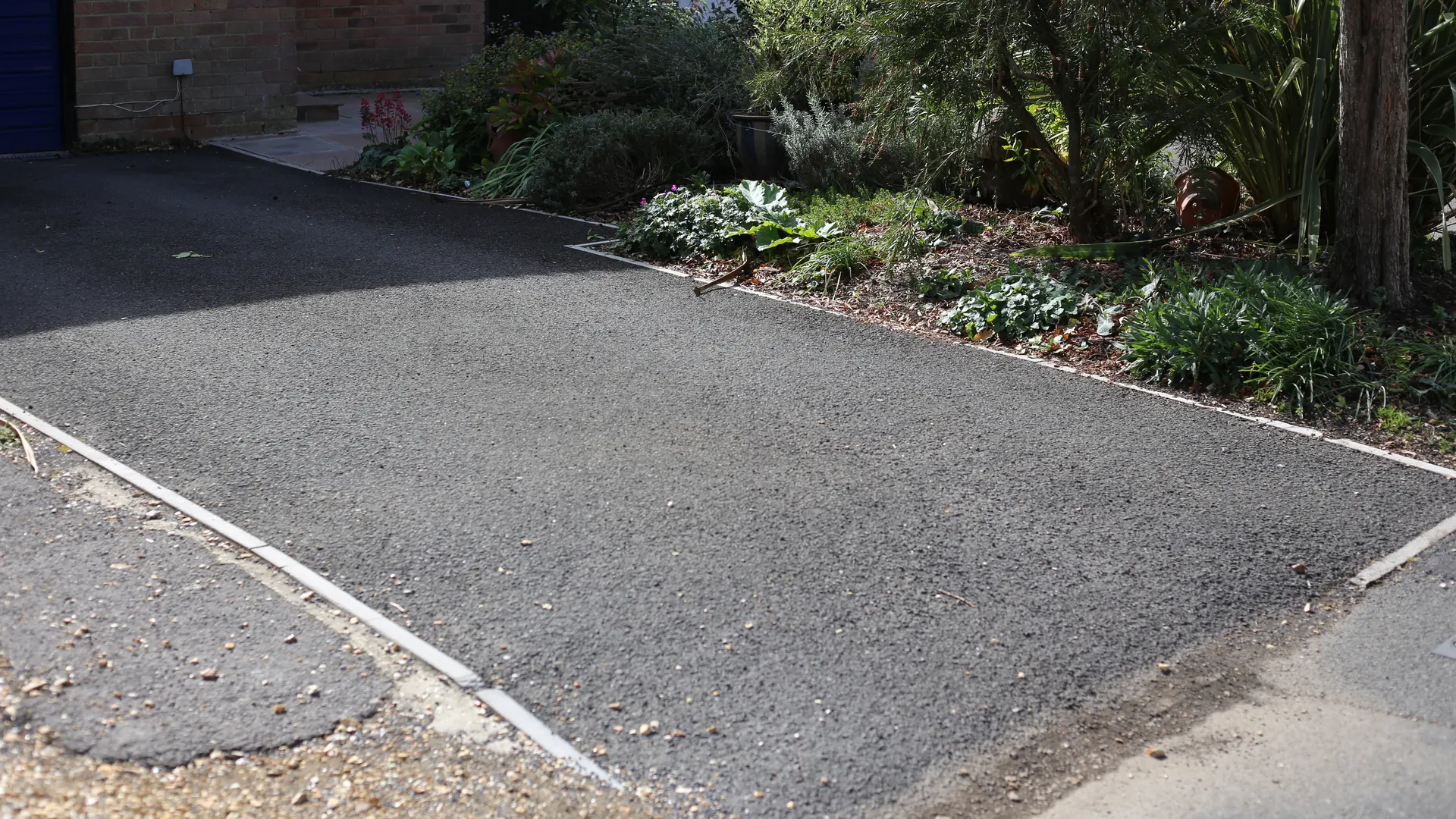 Tarmac driveway with a light kerb edge in front of a brick house